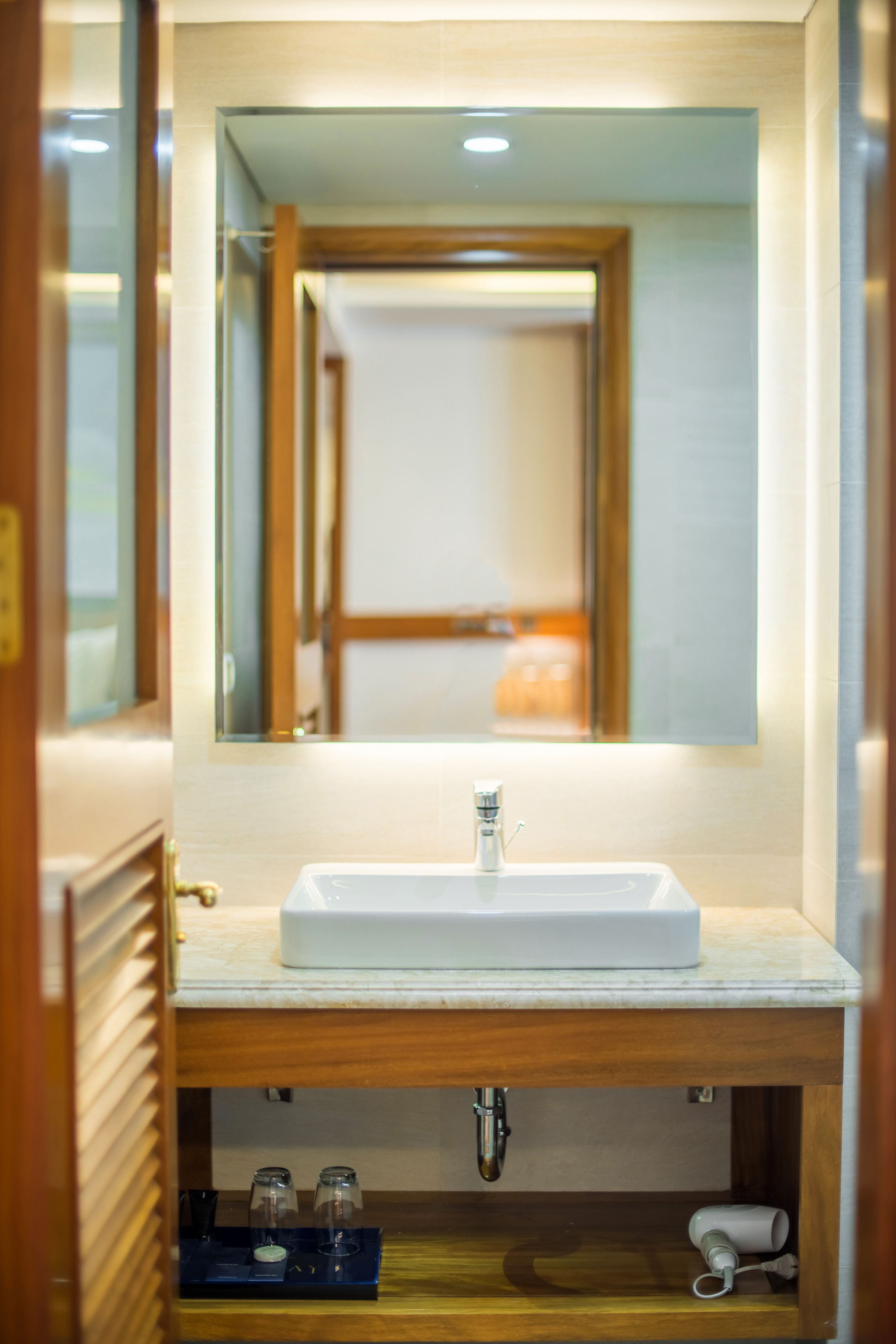 A bathroom with a white sink, wooden vanity, and a mirror above it.