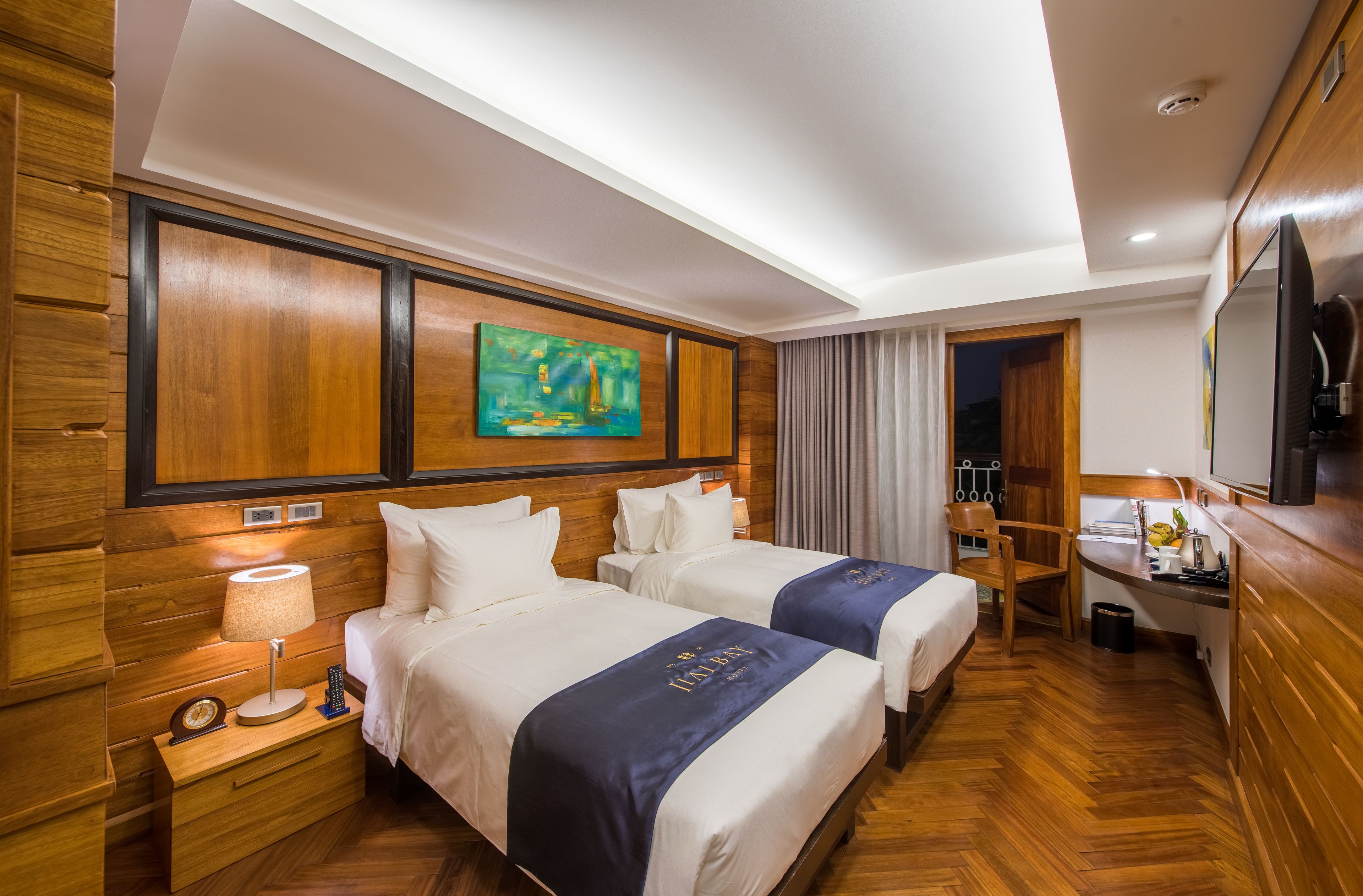 A hotel room with two beds, wooden paneling, a painting, a desk, and a chair.