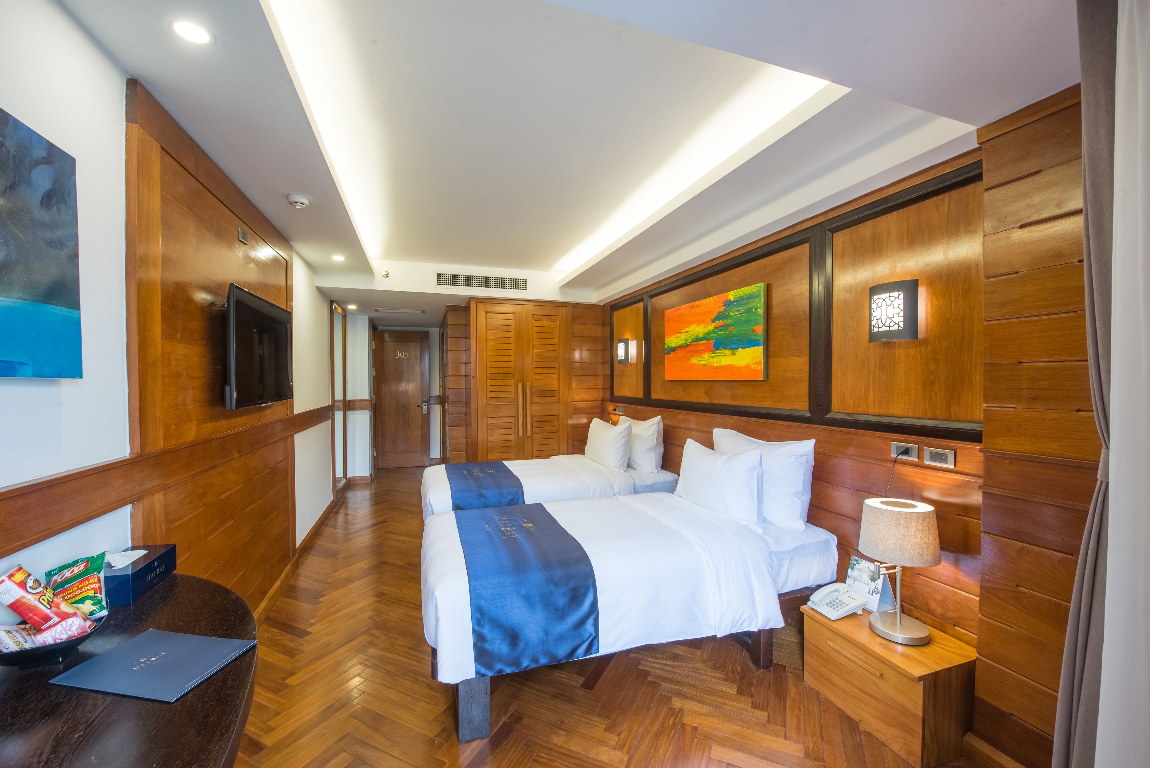 A hotel room with a large bed, a bedside table with a lamp, a TV, and a wooden wall panel.