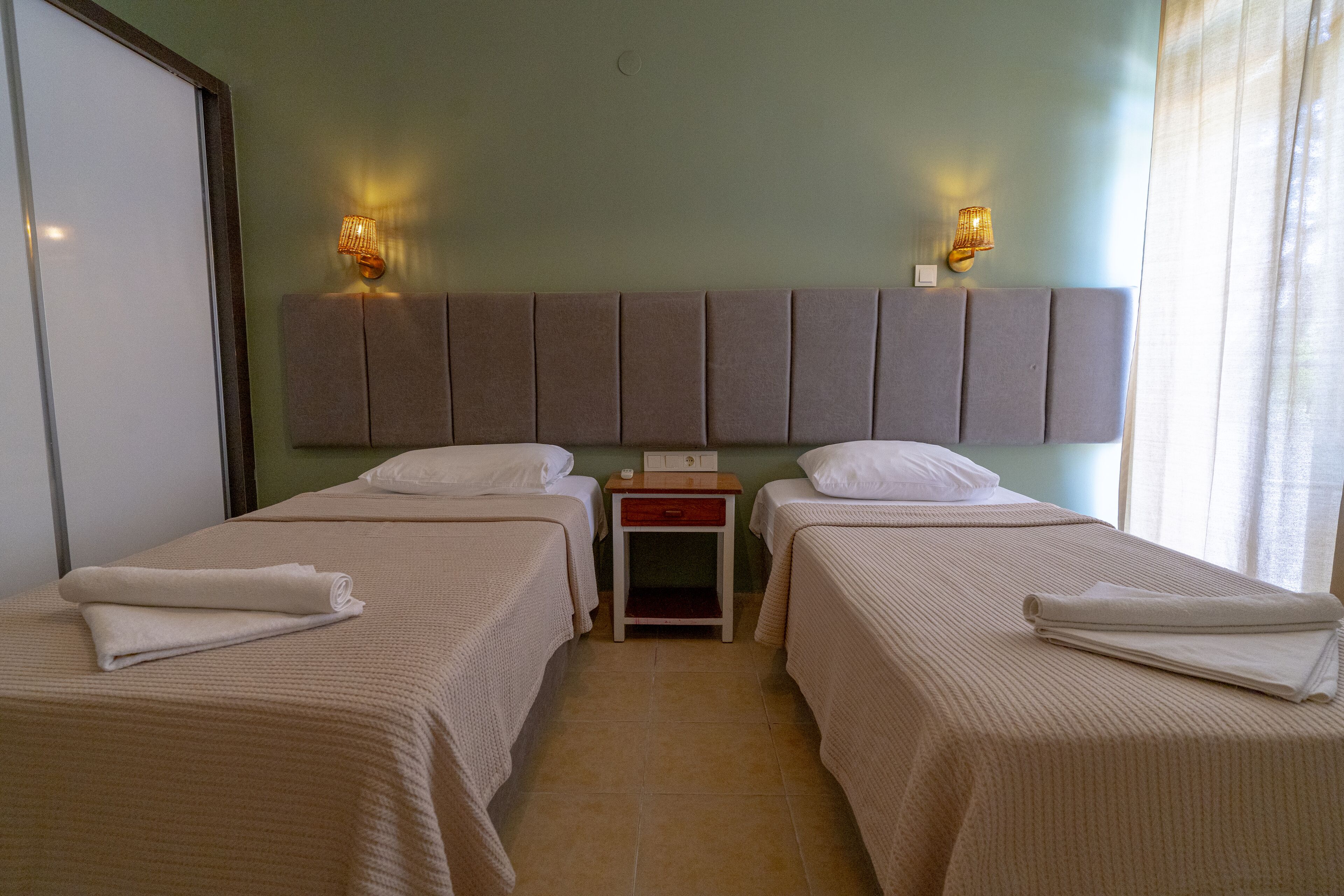 A hotel room with two beds, a nightstand, and two wall-mounted lamps.