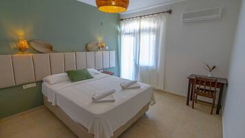 A neatly made bed with white linens and a green pillow, a bedside table with a vase, and a wall-mounted lamp.