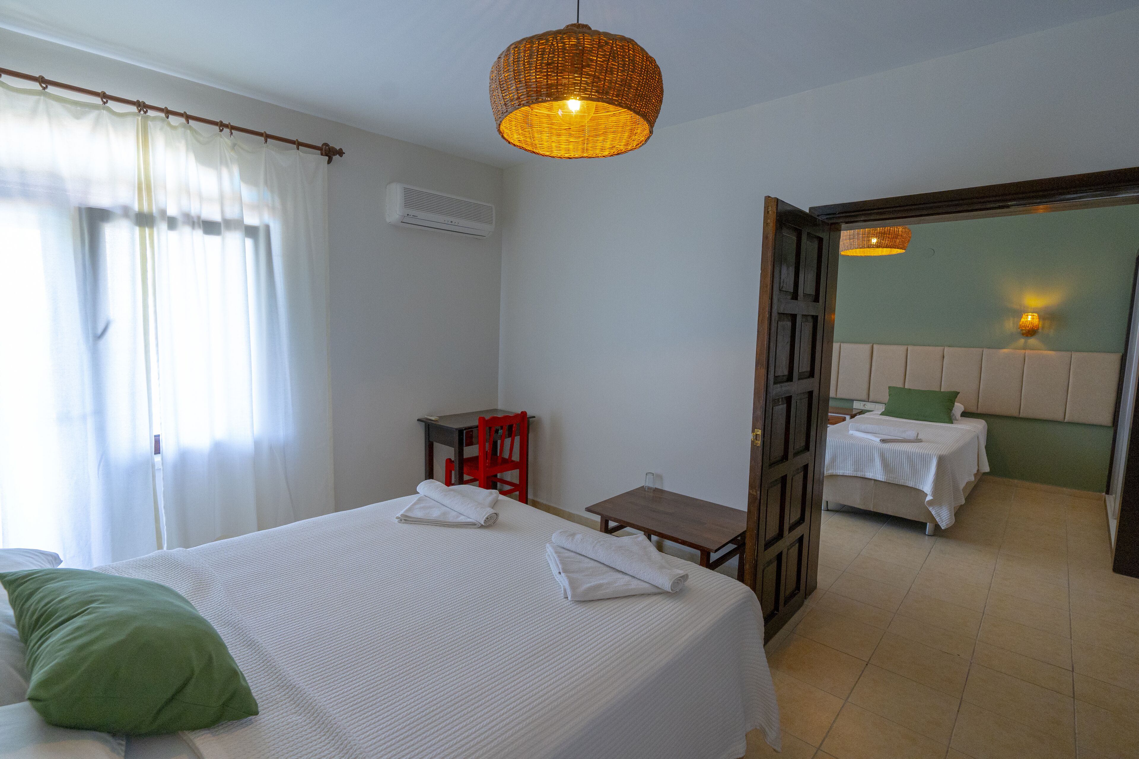 Ein Hotelzimmer mit einem Bett, einem kleinen Tisch, einem Stuhl und einer Tür zu einem weiteren Raum.