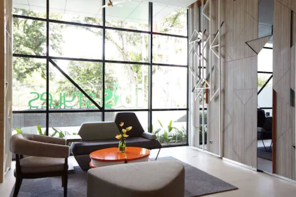 A modern interior with large windows, a sofa, a chair, and a small table with a vase. - ibis Styles Medan Pattimura (Medan)