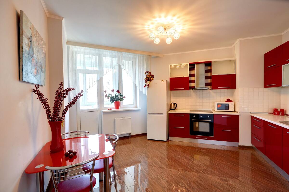 A modern kitchen with red cabinets, a white refrigerator, and a dining area with a red table and chairs.