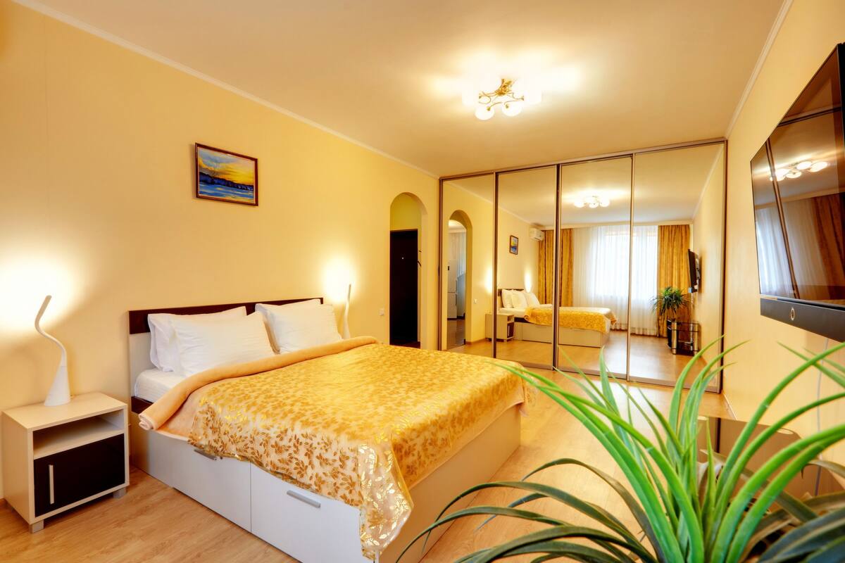 A bedroom with a bed, bedside table, and a large mirror.