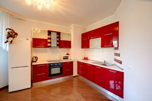 A modern kitchen with red cabinets, a white refrigerator, and a stainless steel sink.