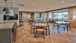 A spacious dining area with multiple tables and chairs, a kitchen in the background, and large windows providing natural light. - Fairfield Inn & Suites by Marriott Albuquerque North (Albuquerque)