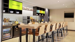 A modern kitchen with a long dining table, a refrigerator, and a microwave. - Home2 Suites by Hilton Elko (Elko)