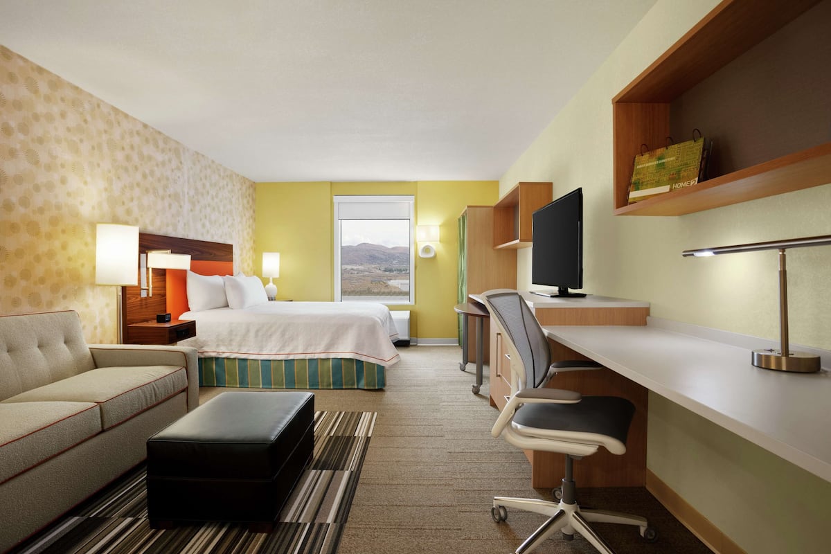 Hotellihuone, jossa on sänky, työpöytä, tuoli, sohva, televisio ja ikkuna, josta on näkymä.