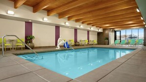 An indoor swimming pool with clear blue water, wooden ceiling beams, and yellow chairs around the pool. - Home2 Suites by Hilton Elko (Elko)