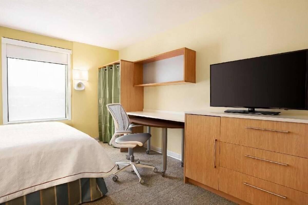Hotellihuone, jossa on sänky, työpöytä, tuoli, televisio ja ikkuna, jossa on verhot.