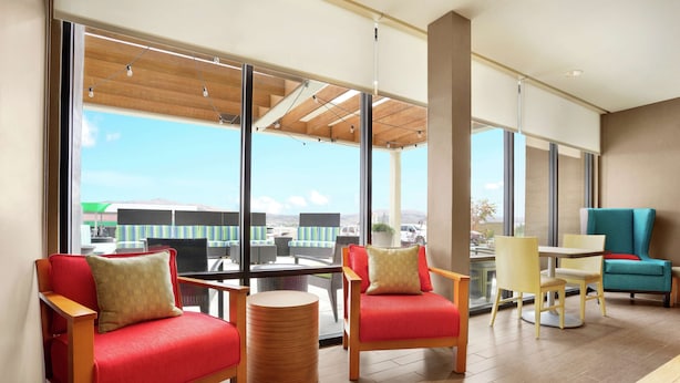 A modern lounge area with red and yellow chairs, a wooden table, and large windows offering a view of the outdoors. - Home2 Suites by Hilton Elko (Elko)