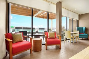 A modern lounge area with red and yellow chairs, a wooden table, and large windows offering a view of the outdoors. - Home2 Suites by Hilton Elko (Elko)