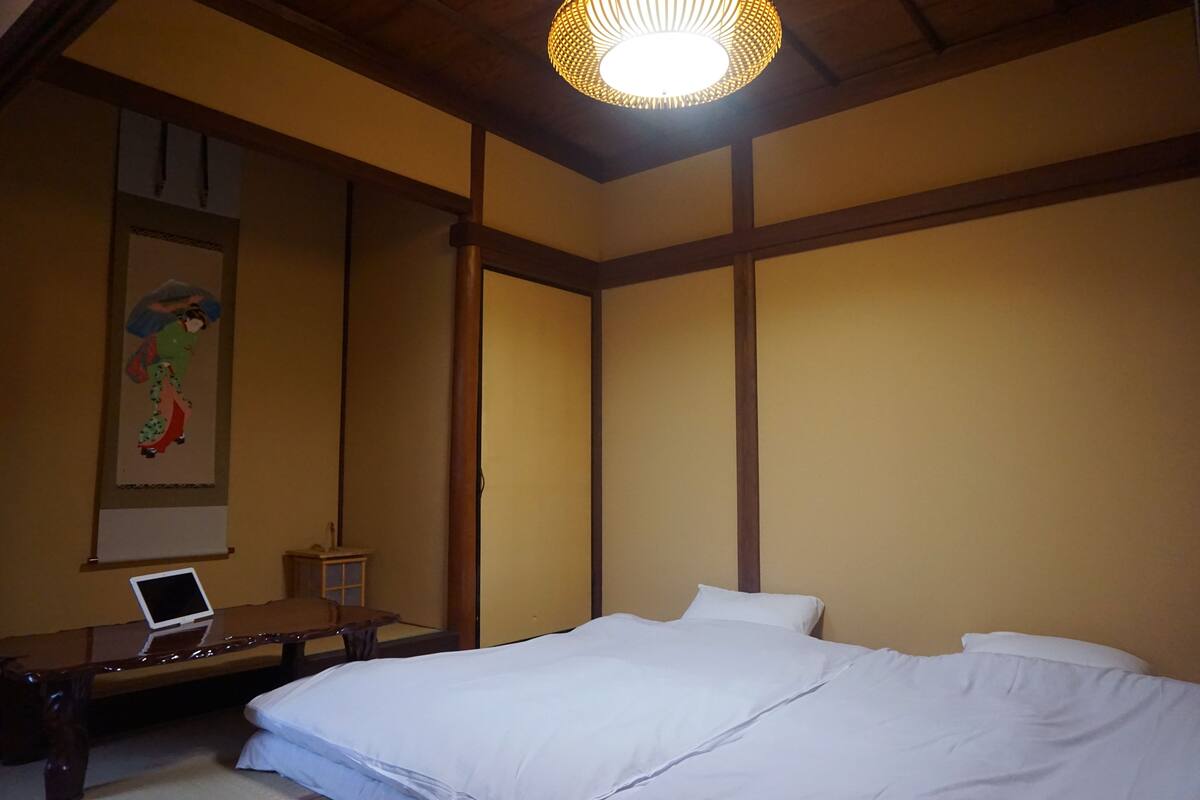 A bedroom with a bed, a desk with a laptop, and a wall-mounted shelf.