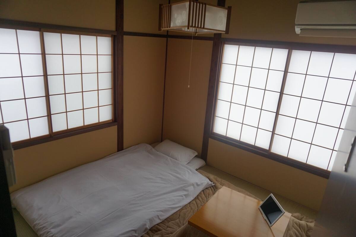 A small, traditional Japanese-style room with tatami flooring, a low bed, and sliding shoji screens.