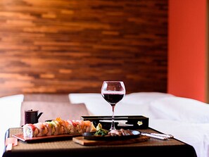 A neatly arranged breakfast tray with sushi, a glass of red wine, and a small cup on a wooden table in a hotel room.