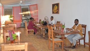 A dining area with wooden tables and chairs, a ceiling fan, and a wall-mounted picture. - Chukwani Executive Inn (Zanzibar Town)