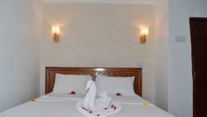 A neatly made bed with a swan towel arrangement, two wall-mounted lights, and a wooden headboard. - Chukwani Executive Inn (Zanzibar Town)