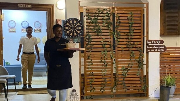 A reception area with a dartboard, a clock displaying time zones, and a sign offering free WiFi. - Chukwani Executive Inn (Zanzibar Town)