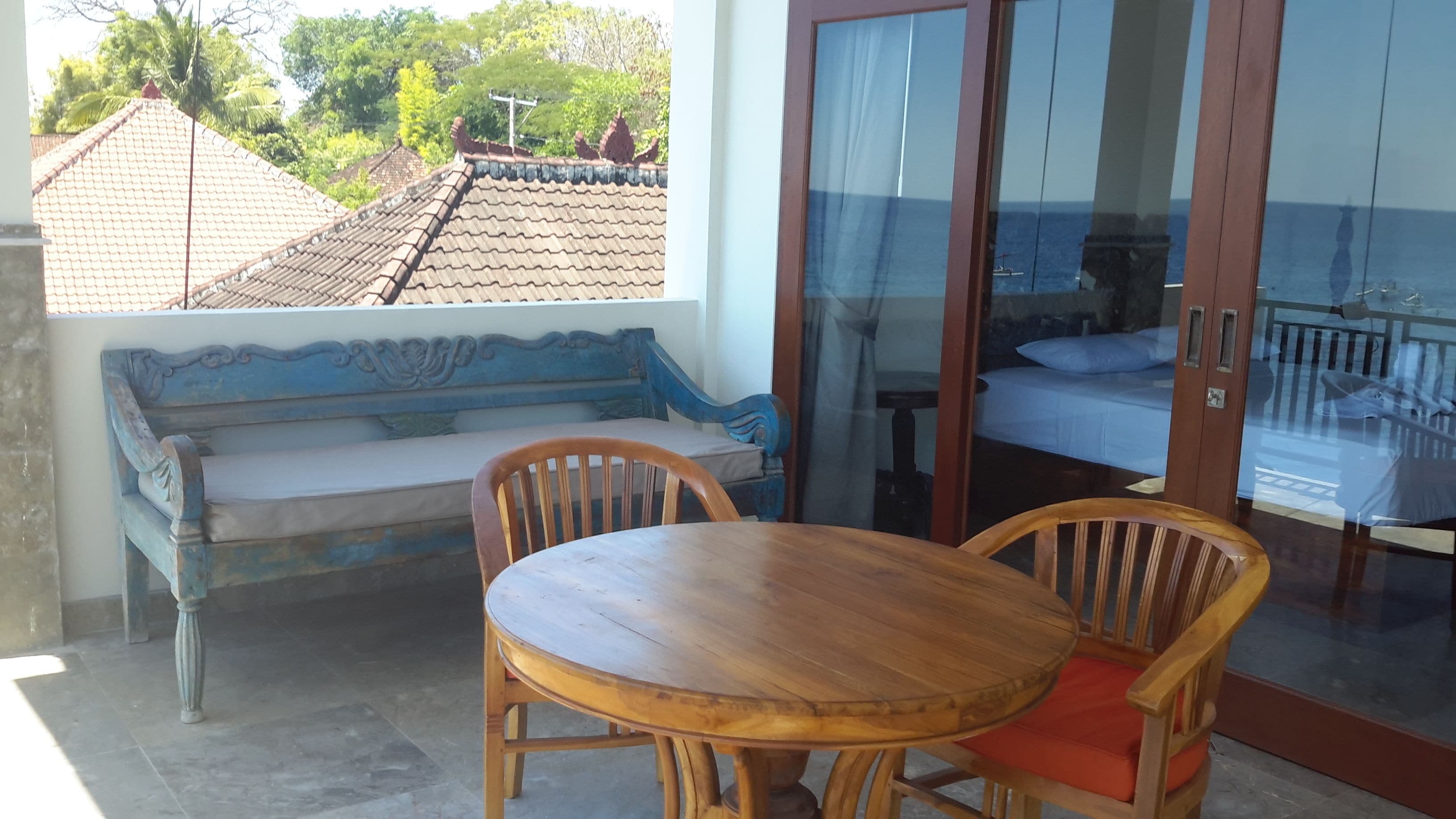 Una mesa y un banco de madera en una habitación con vistas a un tejado de baldosas y vegetación exterior.