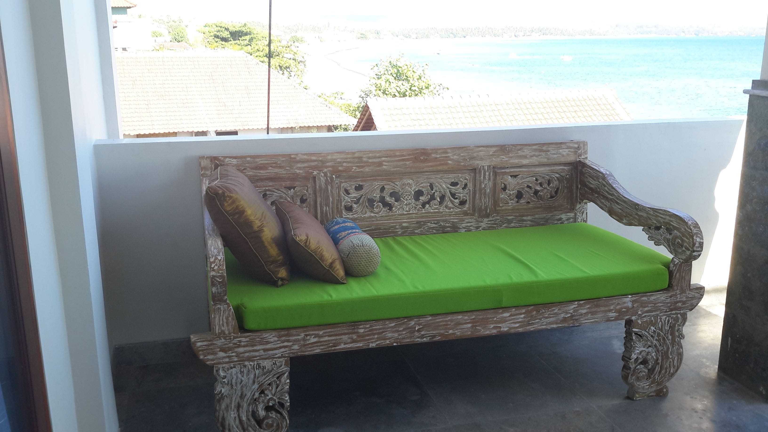 Um banco de madeira com almofada verde, posicionado em frente a uma parede com vista para o mar.
