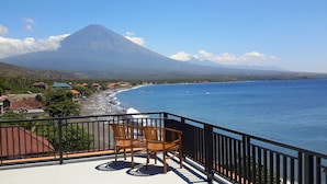 A balcony with wooden chairs overlooking a beach and a mountain. - Amed Beach Villa (Karangasem)