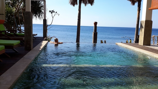 An infinity pool with clear blue water, a wooden deck, and lounge chairs. - Amed Beach Villa (Karangasem)