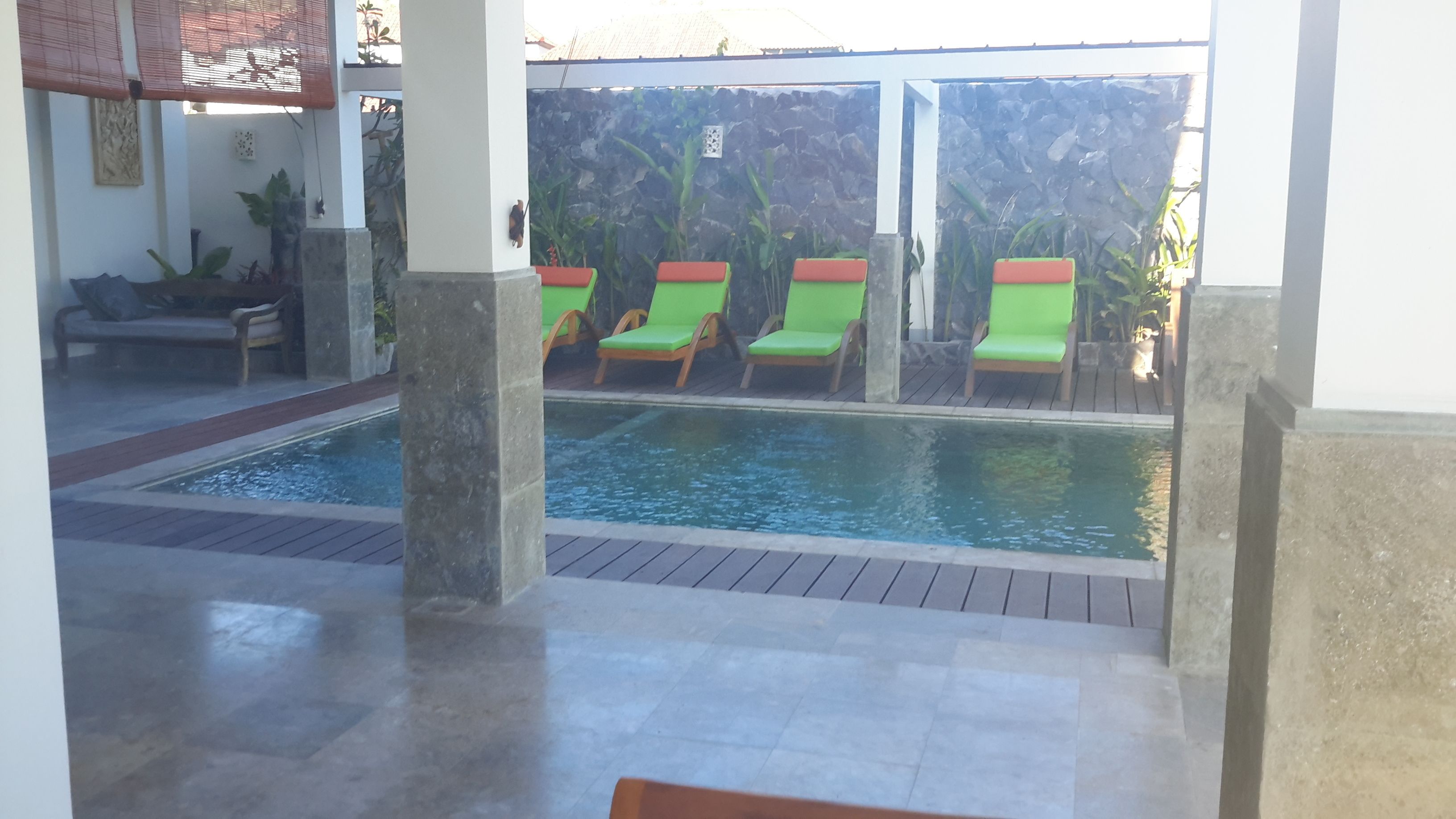 A pool area with a stone floor, green lounge chairs, and a bench.