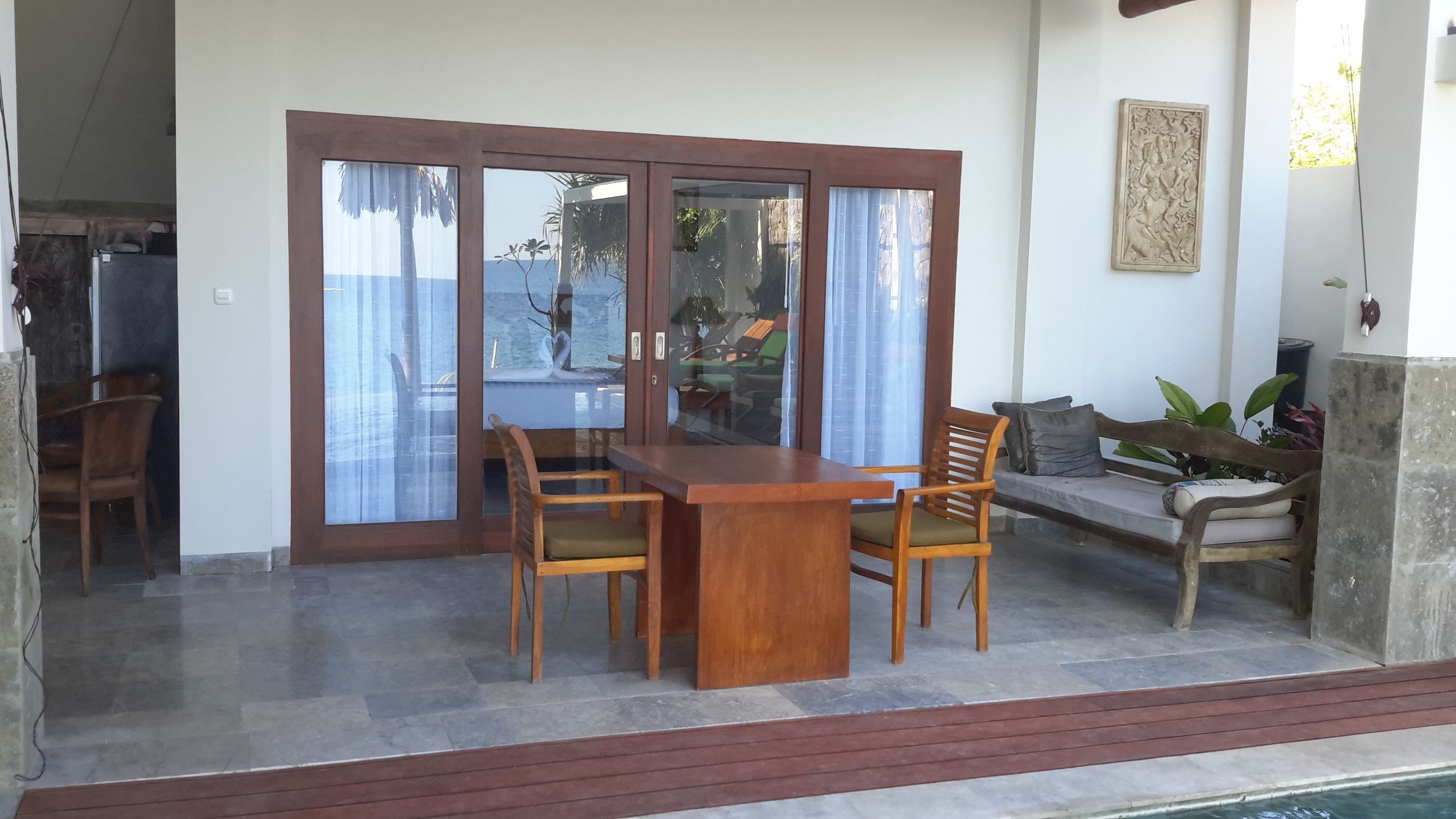 A wooden table with chairs, a sofa, and a glass door leading to a pool area.