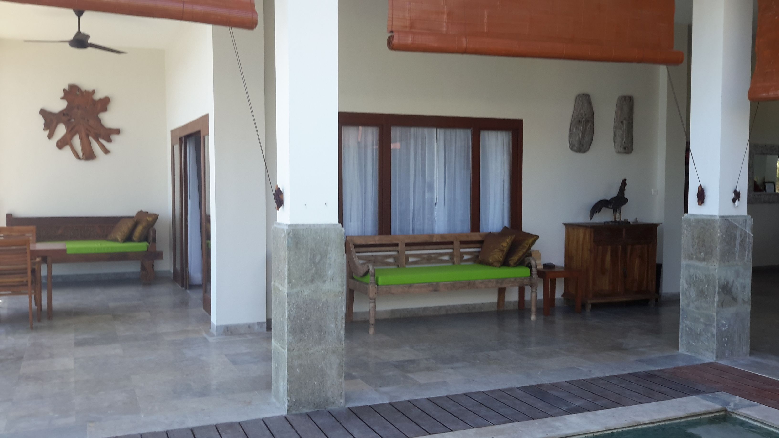 A spacious living area with a wooden bench and a sofa, a ceiling fan, and a view of a pool.