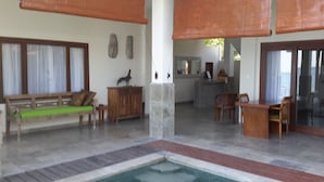 A spacious indoor area with a wooden bench, a small table, and a reception desk. - Amed Beach Villa (Karangasem)