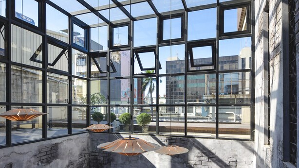 A high-ceilinged atrium with large windows, exposed brick walls, and hanging pendant lights. - Napas Hotel (Taichung)