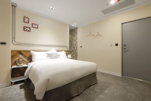A hotel room with a bed, bedside table, lamp, and a door. - Napas Hotel (Taichung)