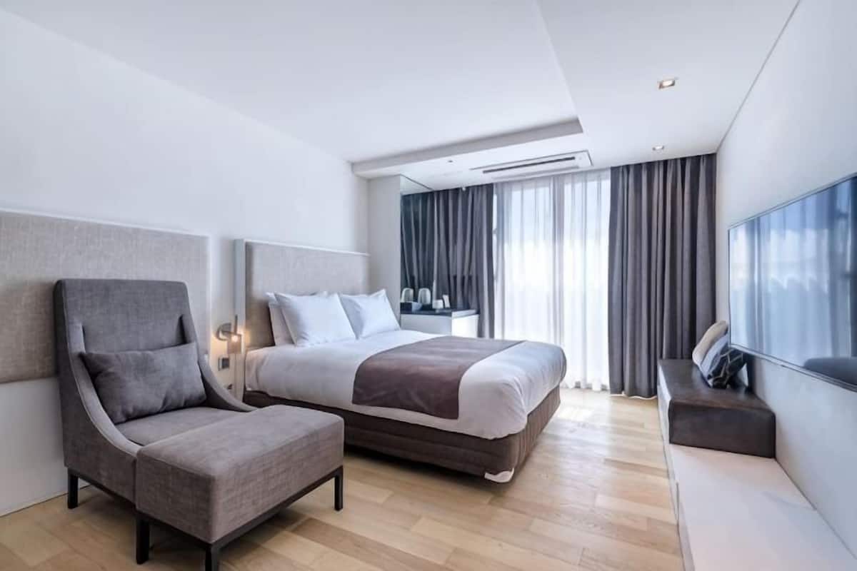 Ein modernes Hotelzimmer mit Bett, Sitzecke, Fernseher und einem großen Fenster mit Vorhängen.