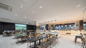 A modern dining area with tables and chairs, a kitchen area with appliances, and a large screen displaying a landscape. - Brown Suites Jeju Hotel & Resort (Seogwipo)