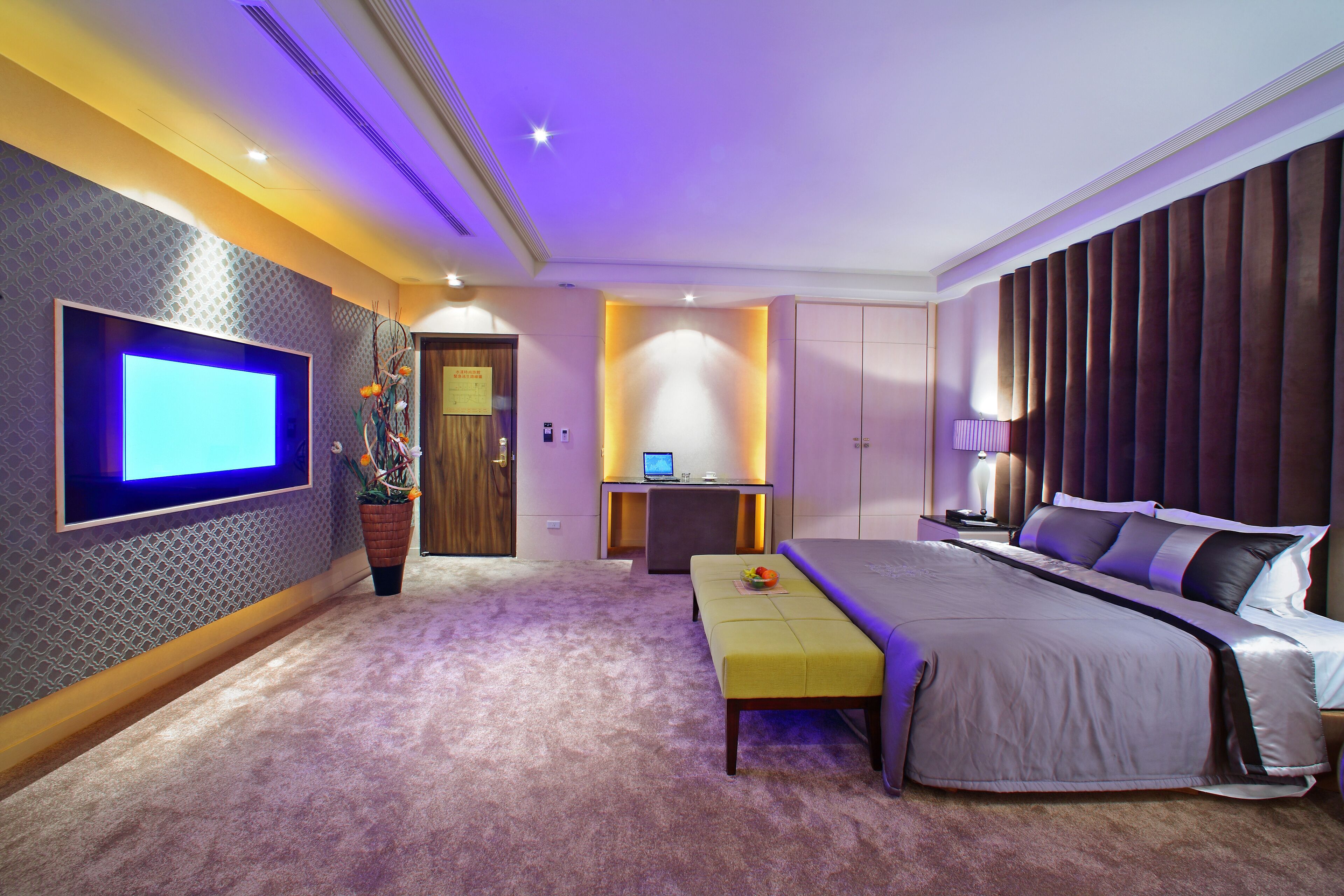 A modern bedroom with a large bed, a flat-screen TV, a desk, and a comfortable seating area.