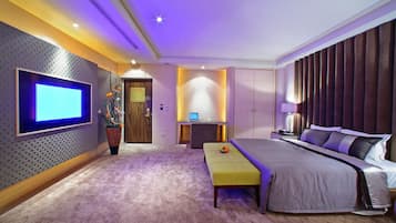 A modern bedroom with a large bed, a flat-screen TV, a desk, and a comfortable seating area.