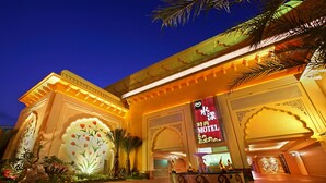 A hotel entrance with a large illuminated sign, decorative arches, and a well-lit pathway.