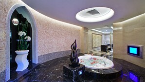 A luxurious bathroom with a marble floor, a large bathtub, a decorative sculpture, and a digital screen.