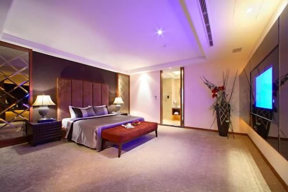 Ein Hotelzimmer mit einem Bett, Nachttischen, einem Fernseher und einer Pflanze.