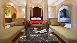 A luxurious bedroom with a large bed, two sofas, a marble coffee table, and a decorative mirror.