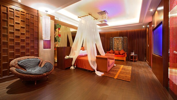 A modern hotel room with a bed, a sitting area, a unique chair, and a television.