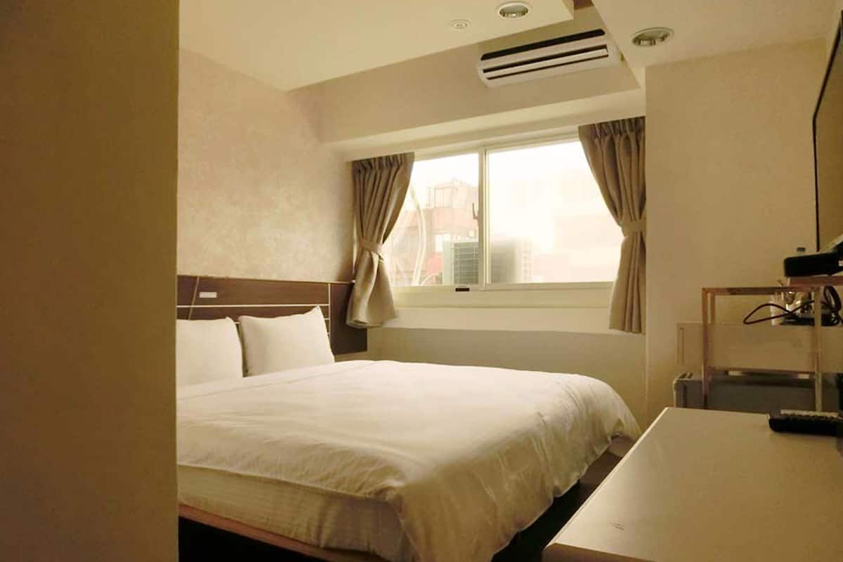A hotel room with a bed, a desk, and a window with curtains.