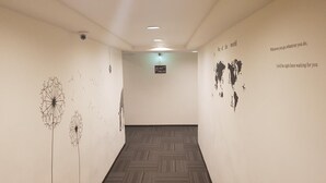 Ein Flur mit einem gemusterten Teppich, Hinweisschildern und Wandbildern von Löwenzahn und einer Weltkarte.