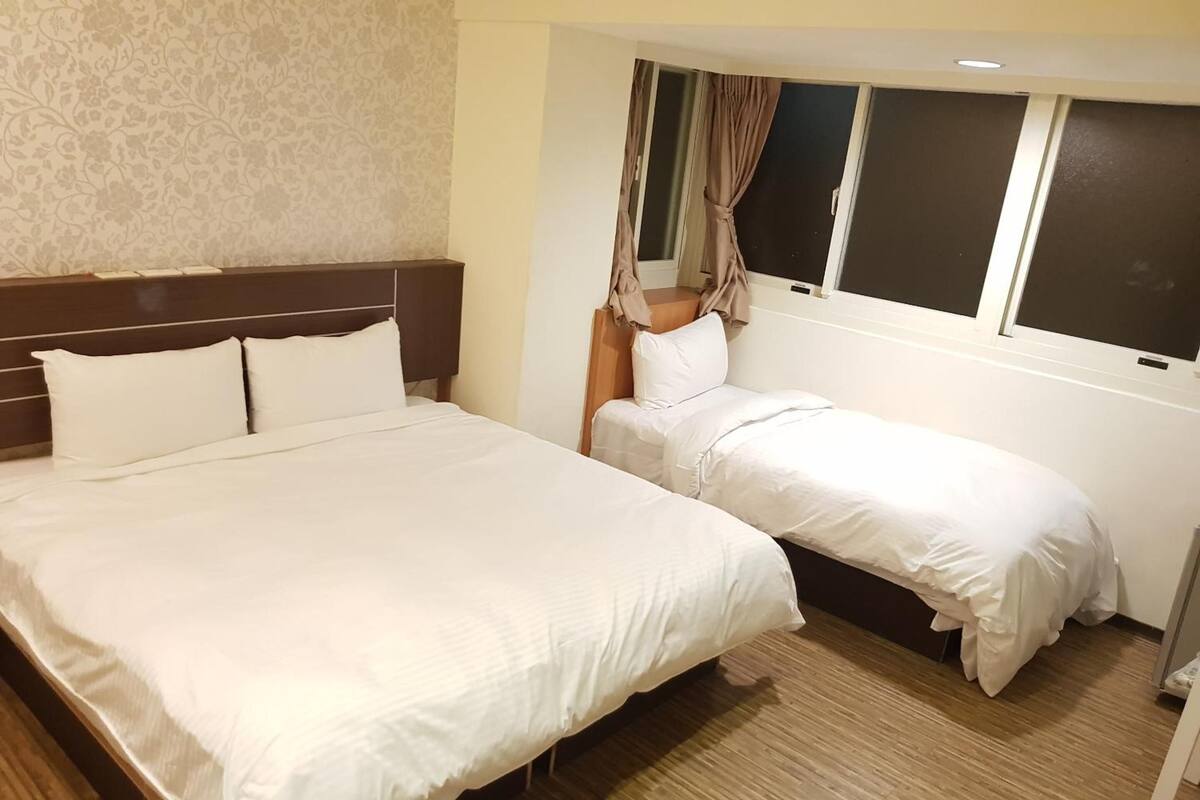 A hotel room with a large bed, a smaller bed, and a window with curtains.