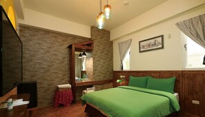 A bedroom with a brick wall, a wooden bed frame, a green bedspread, a wooden desk, a mirror, and a window with curtains.