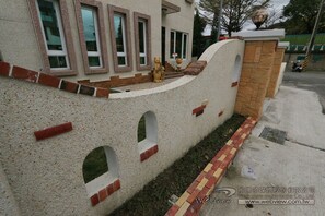 A building with a unique architectural design featuring a wall with multiple small windows and a brick pathway leading to the entrance.