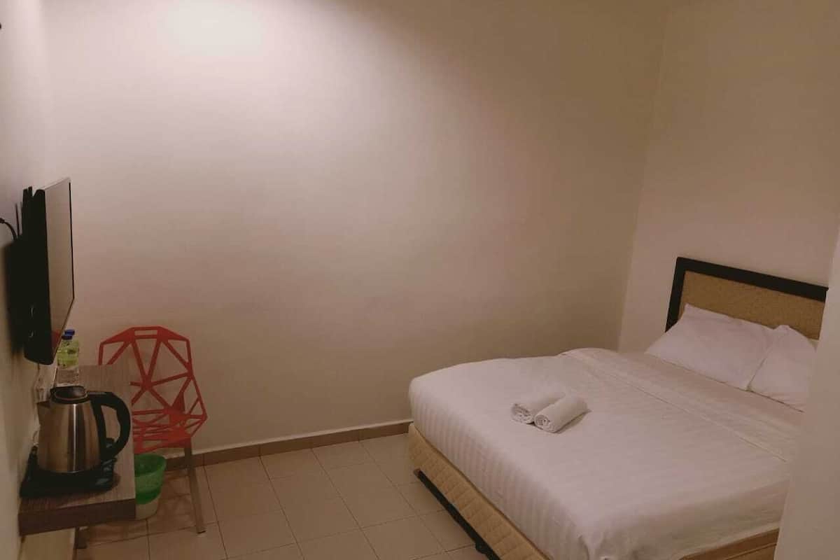 Una habitación pequeña y limpia con una cama, un televisor montado en la pared, una silla roja y una cafetera.