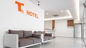 A modern hotel reception area with two sofas, a reception desk, and a large T-shaped sign indicating the hotel's name. - T Hotel Anggerik (Alor Setar)