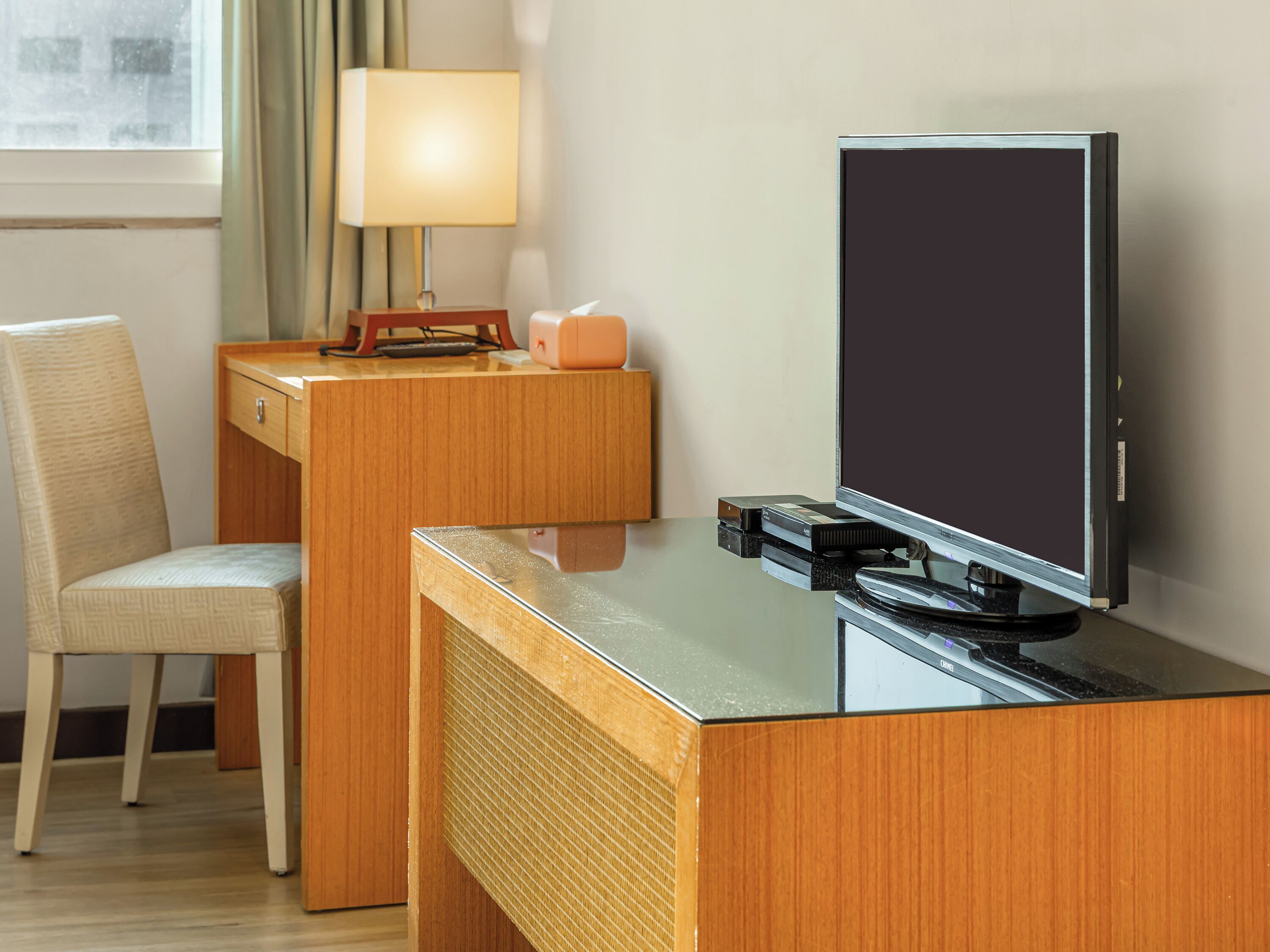Ett hotellrum med ett skrivbord i trä, en stol, en tv och en lampa.